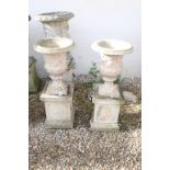 Pair of reconstituted stone garden urns with relief figural classical decoration, raised on square