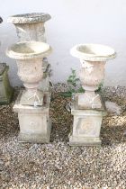 Pair of reconstituted stone garden urns with relief figural classical decoration, raised on square