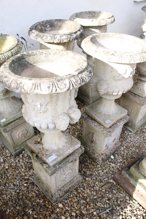 Pair of reconstituted stone garden urns of campana form, with relief facial mask decoration and