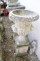 Pair of reconstituted stone garden urns of campana form, with relief facial mask decoration and