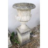 Pair of reconstituted stone garden urns of campana form, with relief facial mask decoration and