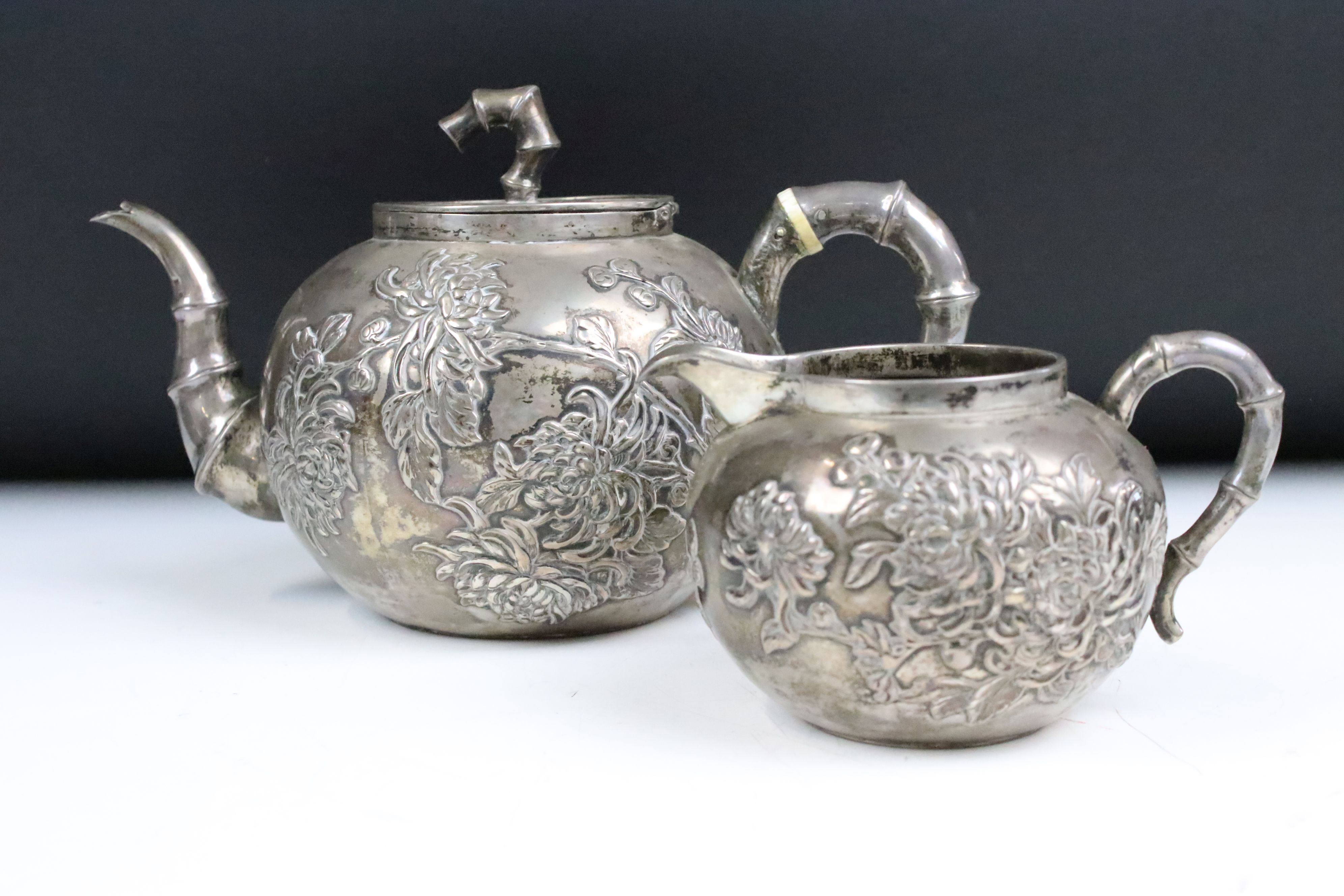 An antique Chinese silver teapot cast with cherry blossom decoration and bamboo style handles and