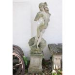 Reconstituted stone statue of a nude maiden stood upon a shell, raised on a square pedestal base.