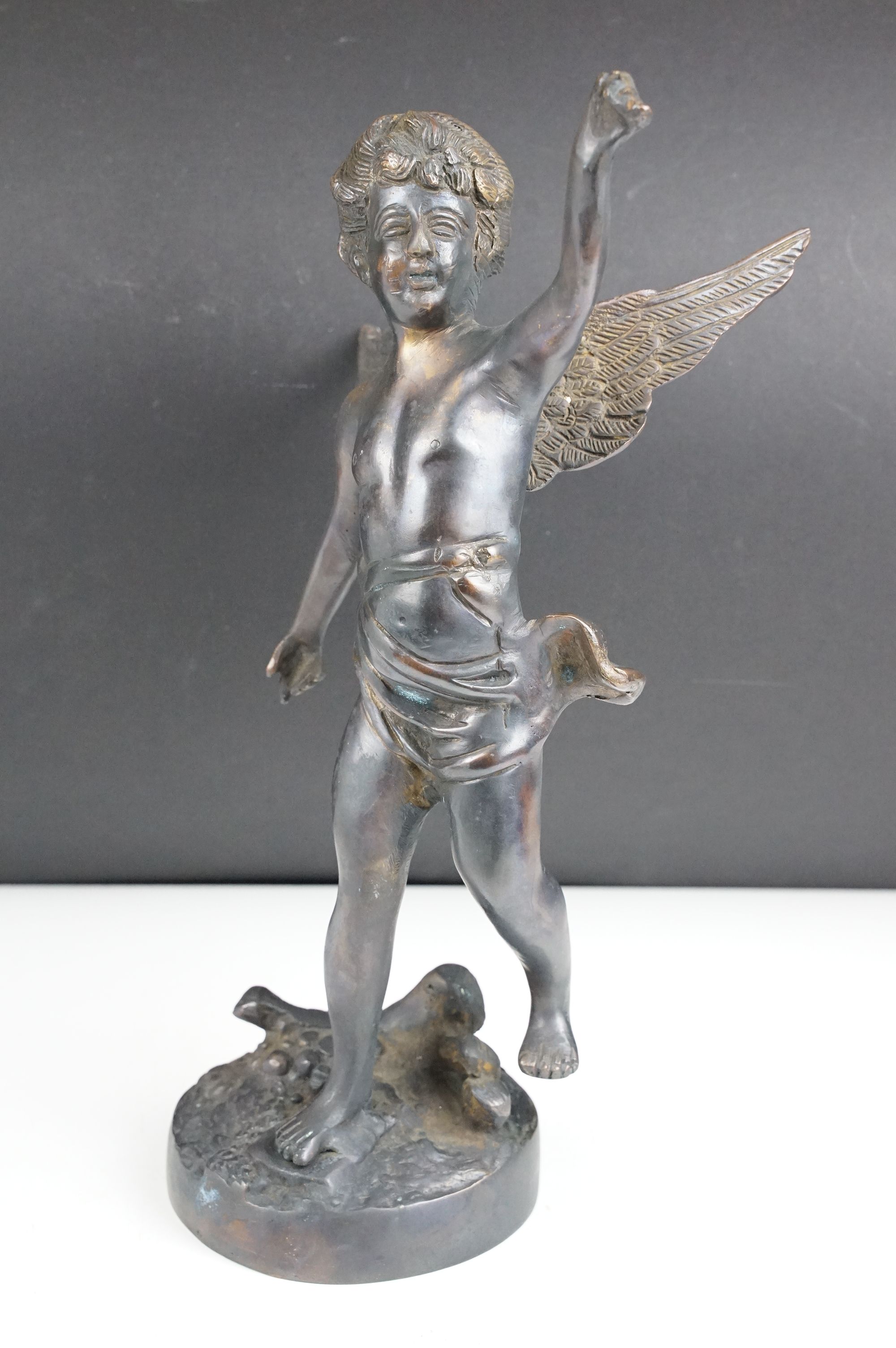 Bronze Cupid / winged cherub sculpture with loin cloth, raised on a circular base of naturalistic