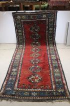 Eastern Wool Rug, the red ground decorated with a line of eight guns within floral pattern border,