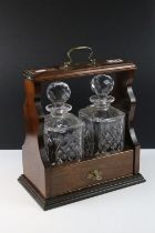 Early 20th century mahogany tantalus with brass mounts, housing a pair of glass decanters &