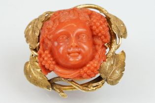 19th century coral yellow metal brooch and earrings; the brooch with carved coral putti face,