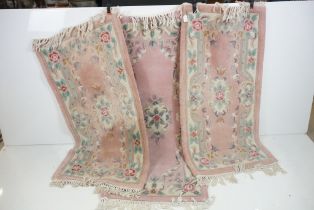 Two Pink Ground Floral Patterned Rugs 130cm x 63cm, together with a similar rug, 152cm x 63cm