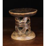 A Small African Tribal Stool carved from heart-wood with a round top above a pierced cylindrical