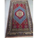A hand knotted woollen rug with a red field - 220cm x 115cm - generally good
