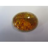 An oval cabochon cut amber (30mm x 22mm)brooch in a bezel setting with ropework boarder - pin and