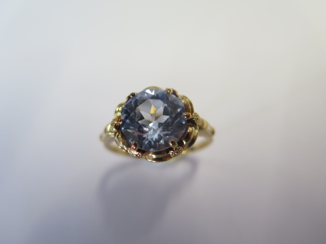 A yellow metal dress ring set with a round 10mm synthetic blue spinel claw set within a looped