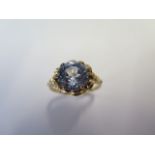 A yellow metal dress ring set with a round 10mm synthetic blue spinel claw set within a looped