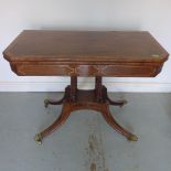 A Regency mahogany and inlaid card table on reeded columns and four outswept legs with brass caps