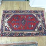 A small hand knotted woollen rug with a red field - 119cm x 72cm - some wear to fringes, colours