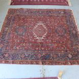 A hand knotted woollen rug with a red field - 185cm x 155cm - some wear mainly to edges otherwise