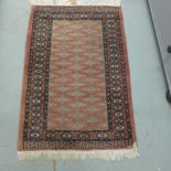 A small hand knotted woollen rug with a pink field - 130cm x 80cm - good condition
