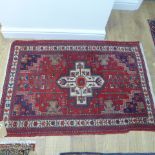 A small hand knotted woollen rug with a red field - 137cm x 90cm - some wear mainly to fringes,