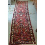 A hand knotted woollen runner with a red field - 295cm x 80cm - generally good condition