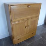 An Ercol Golden Dawn blonde elm cabinet with a drop down front above two cupboard doors and a base