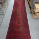 A hand knotted woollen runner rug with a red field, 310cm x 82cm