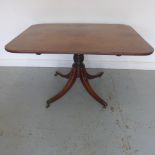 A Georgian mahogany tilt top dining table on four out swept legs with brass caps and casters and a