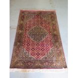A fine woven silk mix rug with a red field, central medallion and stylized boarder - 192cm x 121cm -