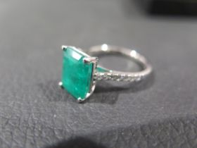 A certified platinum ring set with an octagonal step cut emeralds and round brilliant cut diamond