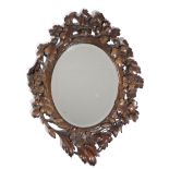 A BLACK FOREST LINDEN WOOD MIRROR C.1900 the oval plate inside a foliate and floral carved and