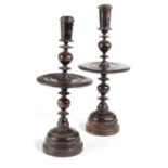 A NEAR PAIR OF TREEN LIGNUM VITAE CANDLESTICKS 17TH CENTURY each with a tapering nozzle above a