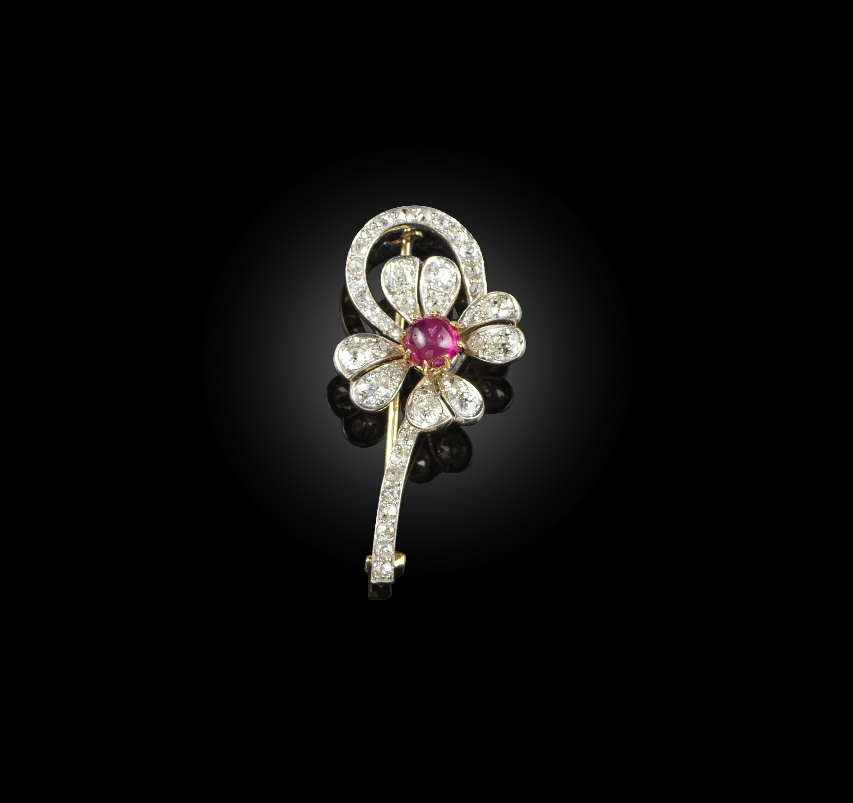 A ruby and diamond brooch, circa 1900, designed as a flower with a curving stem, set with cushion-