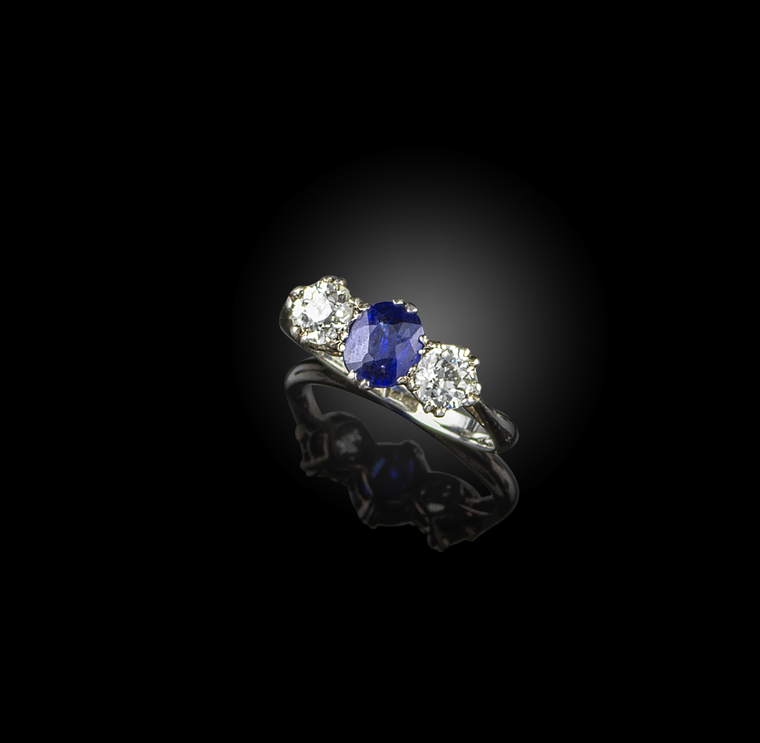 A sapphire and diamond three stone ring, the oval-shaped sapphire set within old circular-cut