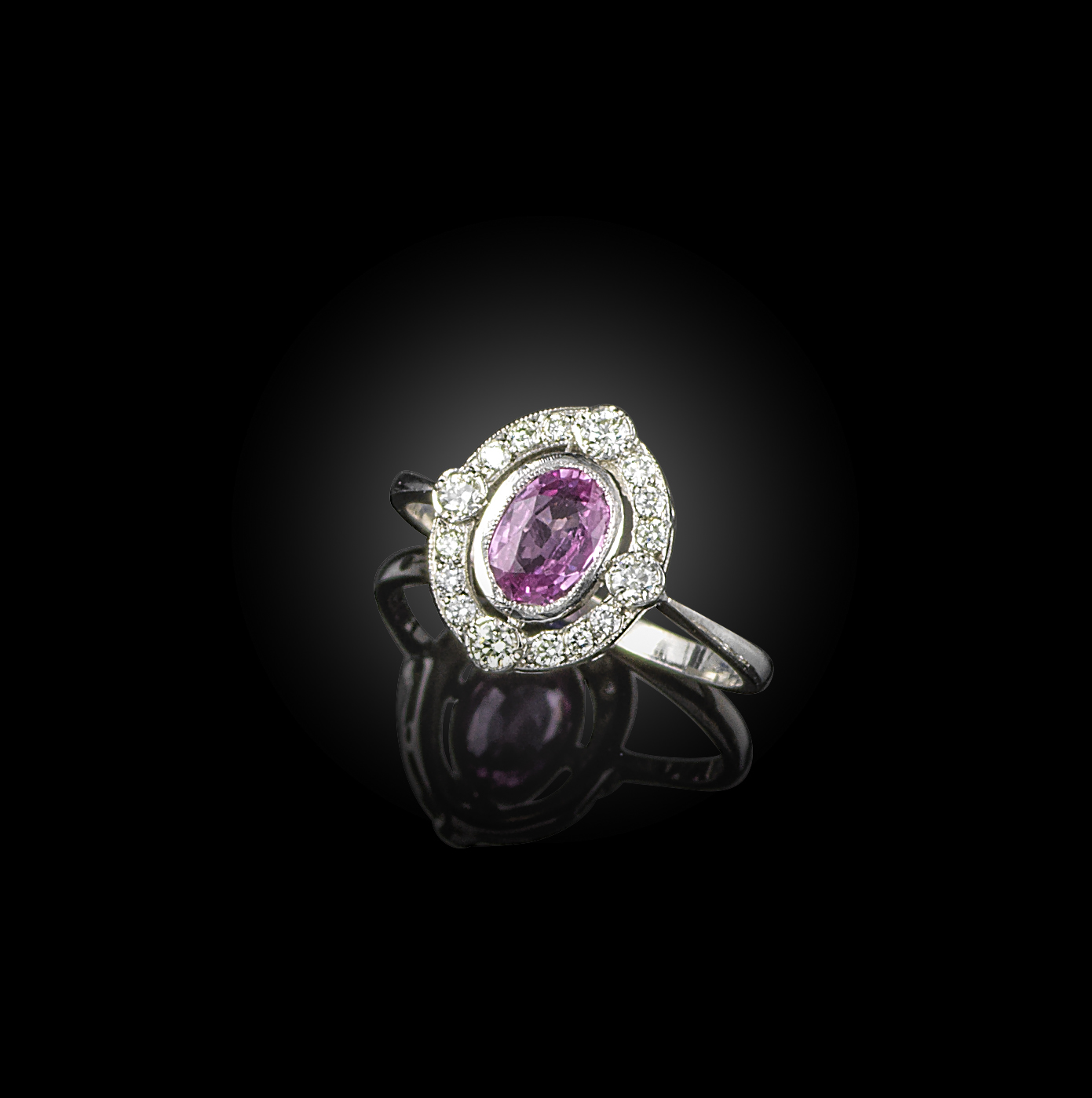 A pink sapphire and diamond ring, of cluster design, set with an oval pink sapphire within an