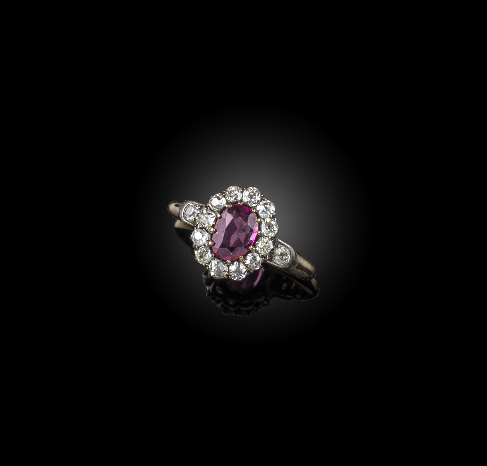 A late 19th century ruby and diamond cluster ring, the oval ruby set within a surround of old