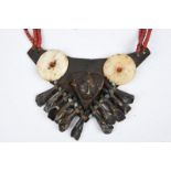 A Naga chest ornament Nagaland with a leather gorget applied shell discs, a brass head, animal teeth