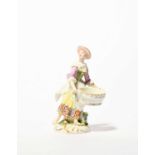 A small Meissen sweetmeat figure, mid 18th century, modelled as a peasant woman carrying a large