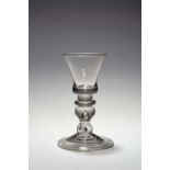 A heavy baluster glass, c.1710-20, the small bell bowl with a solid base raised on a cushion knop