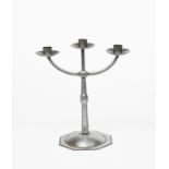 A steel three branch candlestick designed by Ernest Gimson, octagonal, domed base with knopped