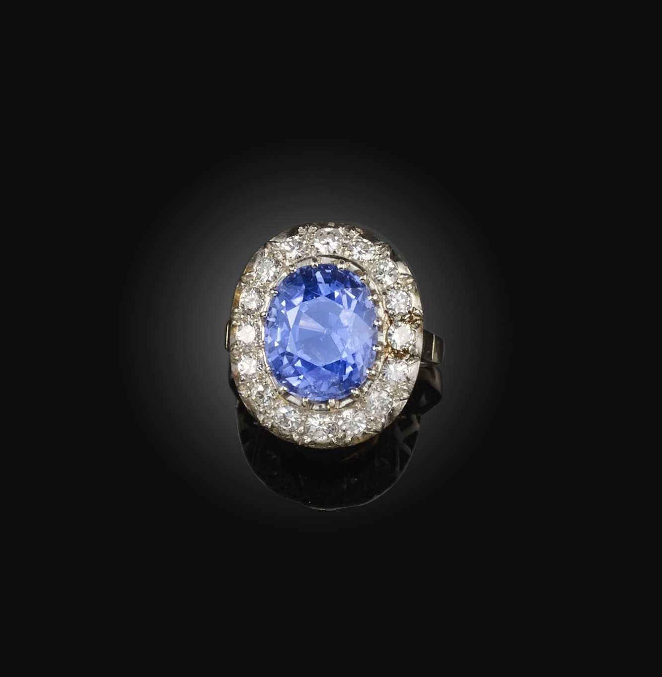 A sapphire and diamond ring, of cluster design, claw-set with an oval sapphire weighing 9.28 carats,