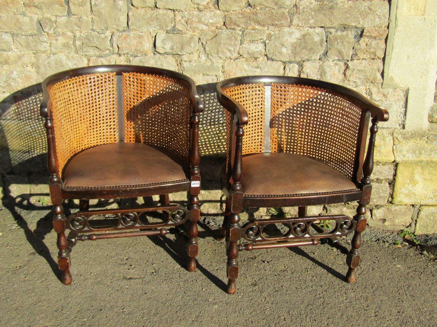 A pair of early 20th century bergere tub chairs with stained beechwood frames, leather upholstered