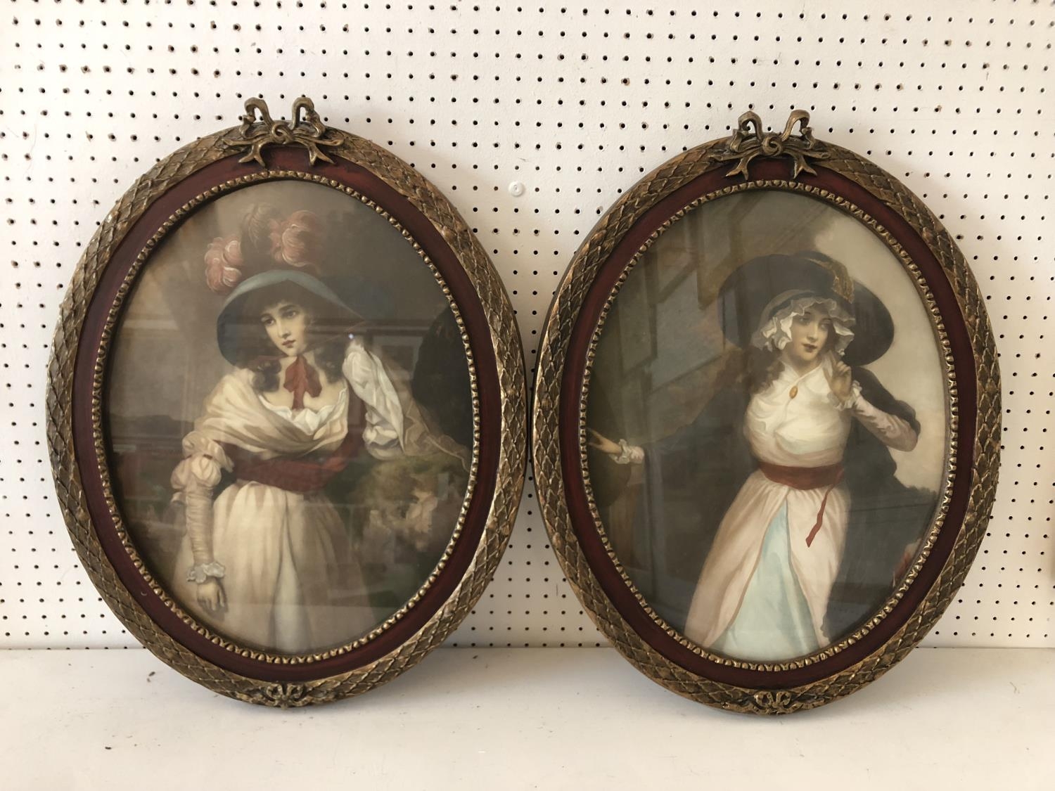 Two c.19th century hand-coloured prints of ladies in hats, in matching decorative oval frames, 44