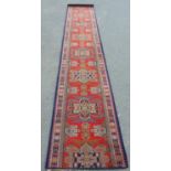 A narrow Kazak style runner within eight medallions on a red ground, 380 x 62 cm approx