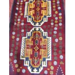 A Baluchi rug with two stepped central medallions on a red field with stylised flowers, 142cm x 86cm