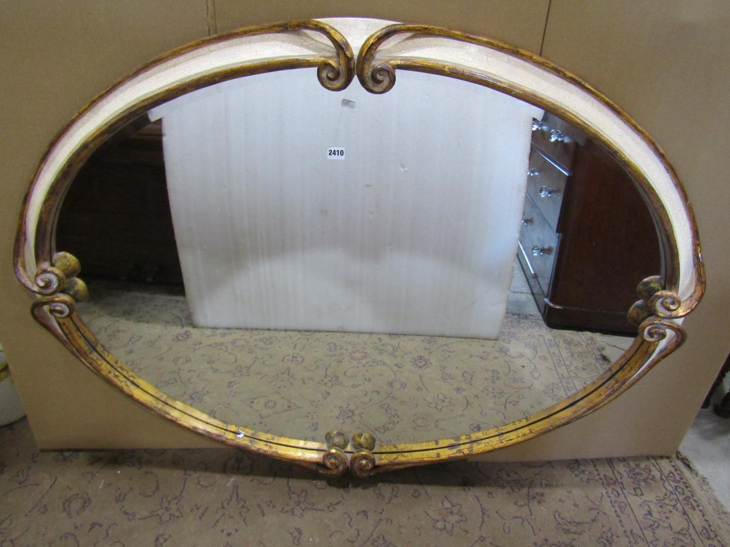 A large oval antique style wall mirror with bevelled edge plate within a scrolled and simulated