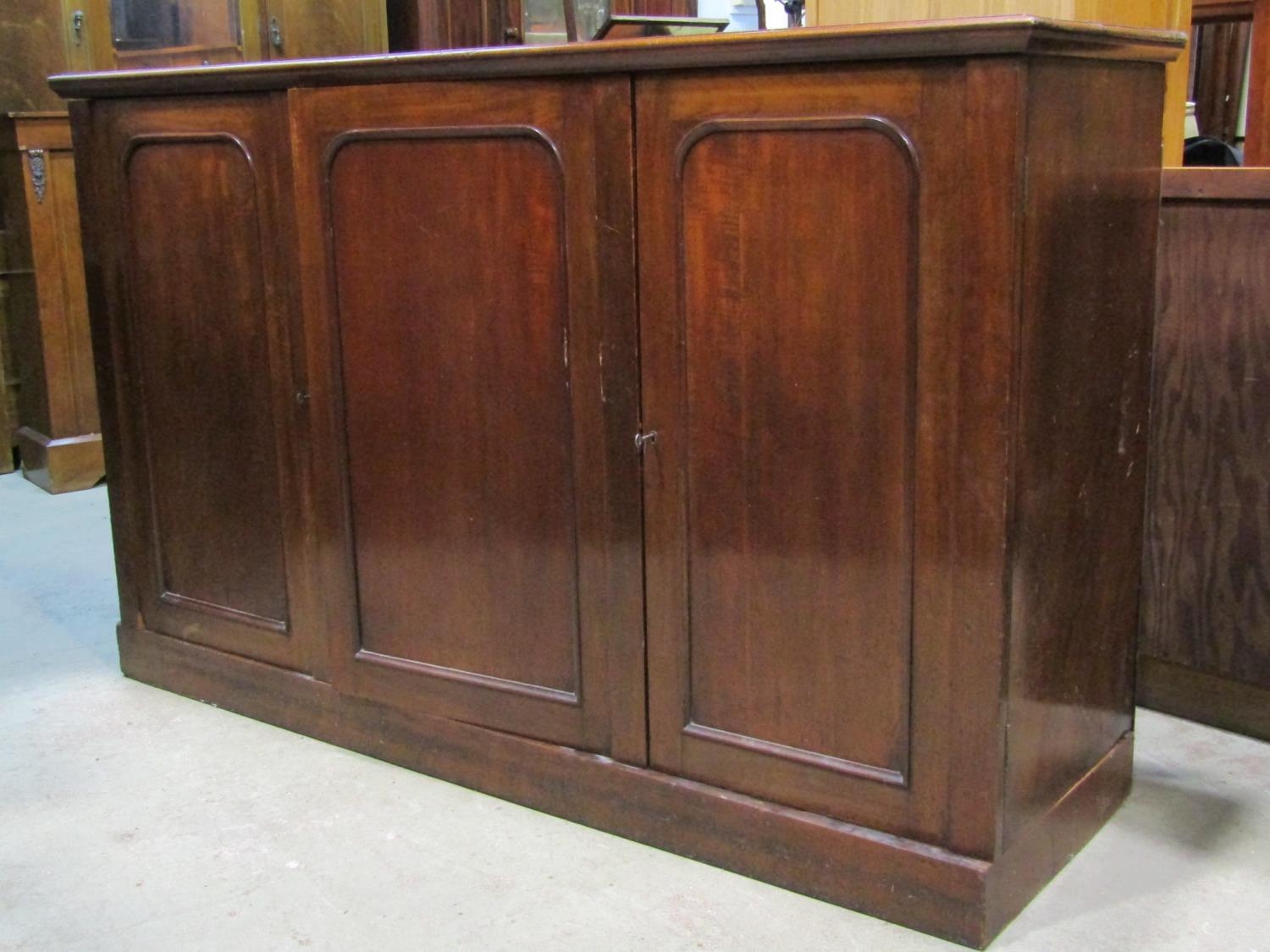 A Victorian mahogany linen cupboard enclosed by three moulded rectangular arched panelled doors, the