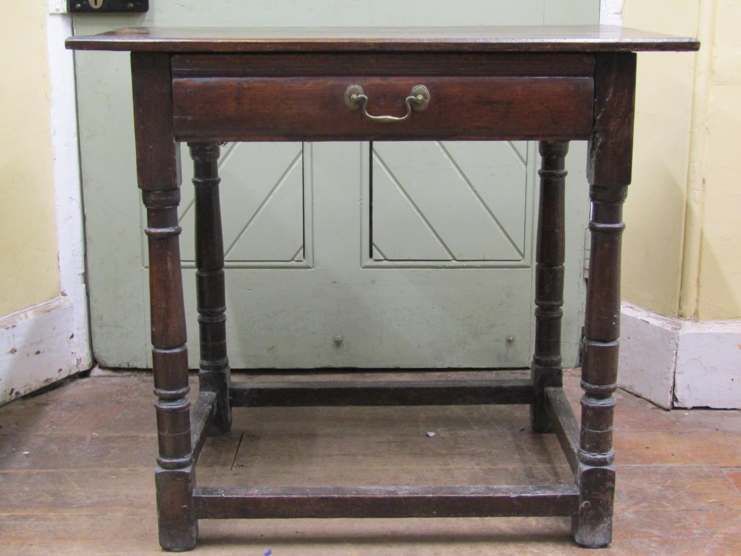 An 18th century oak side table the plank top raised on four turned supports and enclosing a frieze