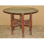 An Eastern engraved circular brass tray top occasional table raised on a folding wooden stand 70