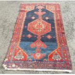 An old Kazak carpet with a central extended medallion and stylised flowers on a dark blue ground,
