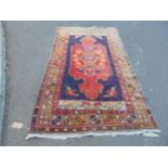 A middle eastern design carpet with a central scrolled medallion on a red ground and purple