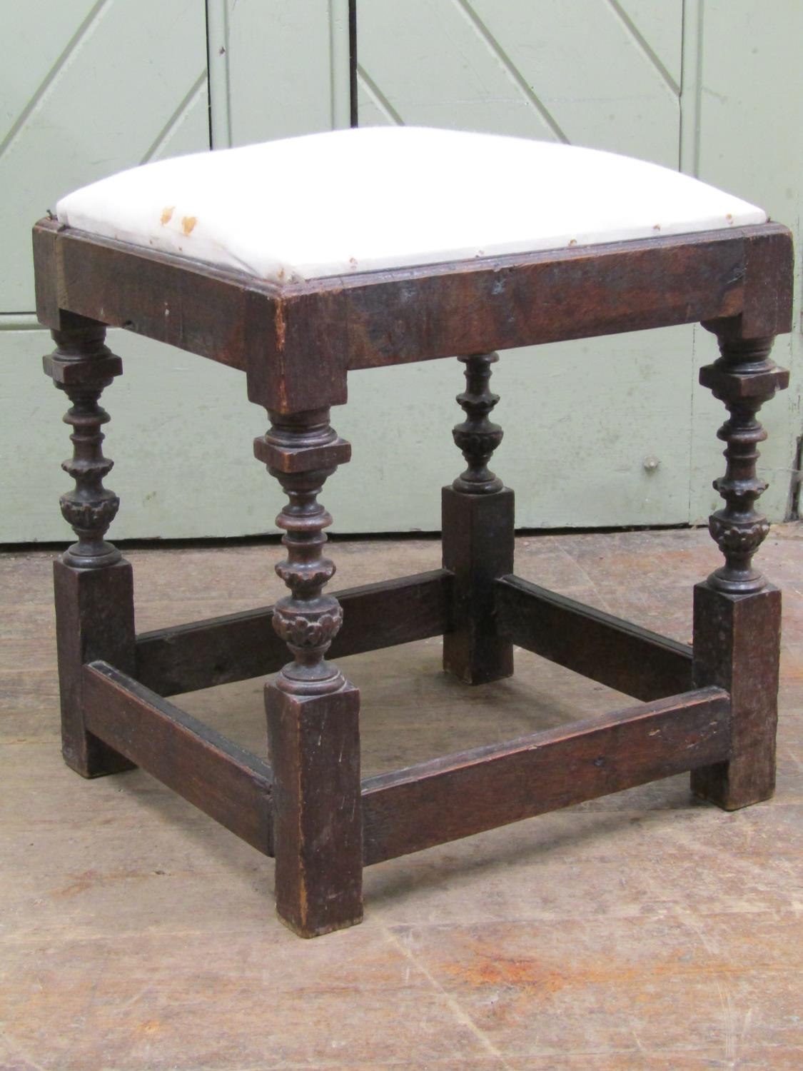 An antique oak stool with upholstered top raised on four turned and carved supports